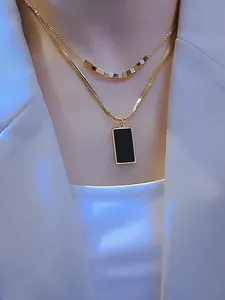 Detalle del collar de capas en titanio dorado con cadena de serpiente y colgante cuadrado negro