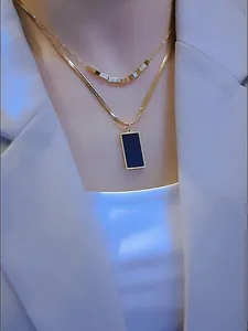 Collar de doble capa dorado con cuentas cuadradas y colgante negro sobre un traje blanco