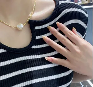 Detail of a baroque pearl pendant on a gold flat snake chain worn by a model