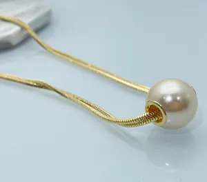 Macro detail of a round white pearl pendant on a sleek golden snake chain necklace