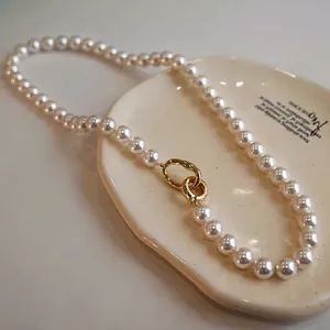 Détail de perles rondes blanches avec un fermoir en métal doré unique sur un plat en grès