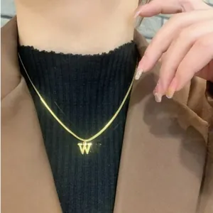 Dettaglio di una collana a serpente dorata con ciondolo lettera W su modella donna