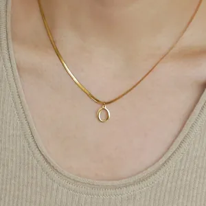 Dettaglio della collana piatta dorata con ciondolo a lettera O su una modella