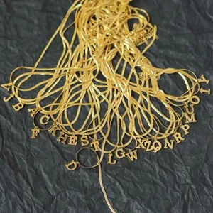 Primo piano di 26 ciondoli con lettere dorate su catene a serpente piatte su sfondo nero