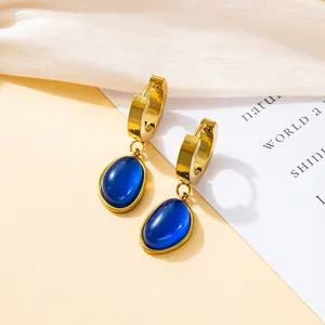 Detail of gold dangle earrings with oval blue opal stone on soft fabric background