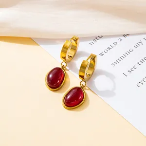 Retro gold hoop earrings featuring elegant red oval gemstone pendants on a cream fabric backdrop