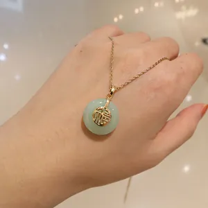 Détail d'un collier vintage doré avec pendentif en jade vert rond et motif caractère Fu