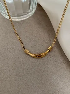 Macro shot of gold curved bar necklace with tiger eye stone on a textured grey surface