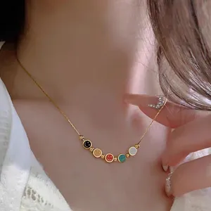 Dettaglio di una collana dorata con cinque ciondoli smiley in smalto colorato su modella