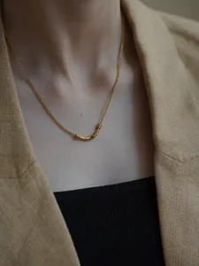 Detail of 18K gold plated minimalist necklace with a curved cylindrical pendant on a model
