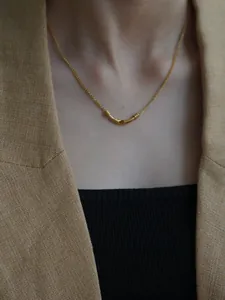 Close-up of golden necklace with curved tube pendant on a model wearing a camel suit