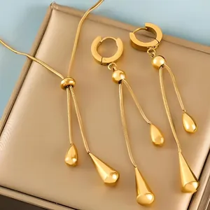 Close-up of golden teardrop pendant necklace and tassel earrings set on display tray