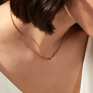 Close-up of gold chain necklace featuring an arc pendant with blue gemstone inlay on model