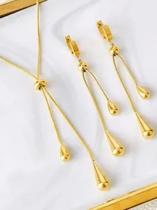 Close-up of golden teardrop fringe earrings and snake chain necklace on marble tray