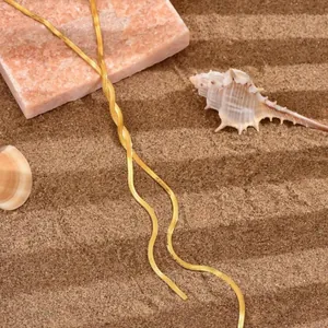 Close-up of golden herringbone snake chain necklace on sand with shells