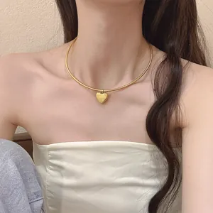 Elegante goldene Herzkette an einem Model mit einer polierten Schlangenkette im Choker-Stil