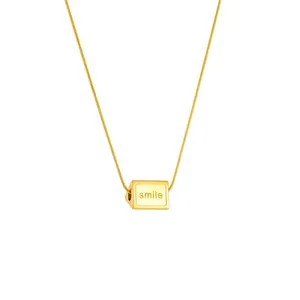 Macro shot of gold cube pendant engraved with smile text on a delicate link chain
