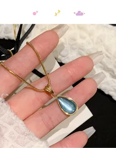 Detailed close-up of gold snake chain necklace with blue teardrop gemstone pendant