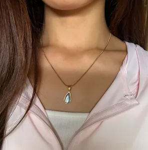 Detail of a gold teardrop necklace with blue gemstone on model wearing a pink jacket