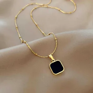 Collier doré minimaliste avec pendentif carré noir sur fond en soie de luxe champagne