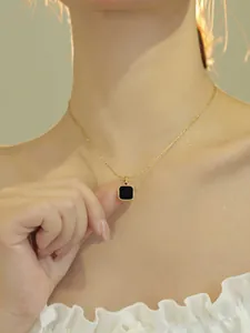 Gros plan d'un collier doré avec pendentif carré noir sur le cou d'une femme