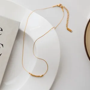 Detail of minimalist double-layered golden beaded necklace with cube charms on ceramic plate