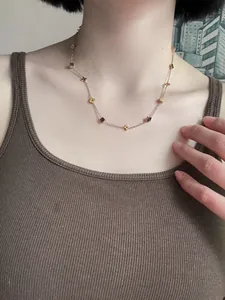 Detail of rose gold clover and square charms on a slim steel chain worn on the neck