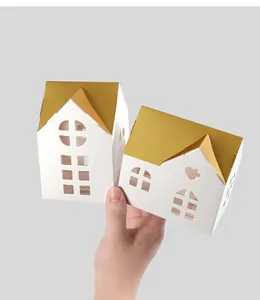 Close-up of hollow white paper favor boxes with golden roofs held in hand