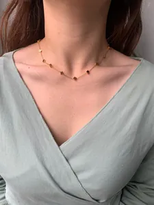 Detailed view of a gold clover necklace with mini cubic charms on a model's neck