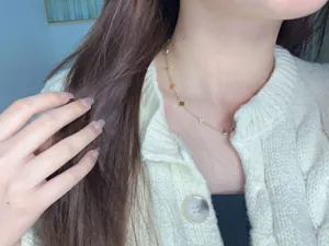 Detailed view of a gold four-leaf clover necklace worn over white knitwear
