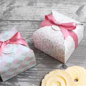 Close-up of small square gift boxes with fan patterns and pink satin ribbons on a rustic table