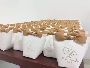 Detail of white leather wedding favor bags with brown bows and custom names on wood surface