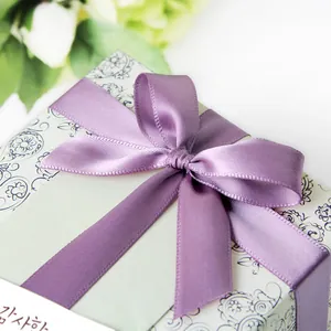 Light purple satin ribbon tied in a bow on a floral gift box with a thank you card
