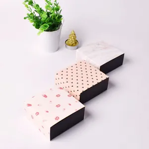 Drei quadratische Geschenkschachteln mit Marmor-, Herz- und Erdbeermustern auf weißem Tisch