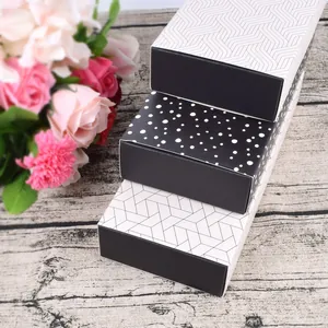 Three square cardboard gift boxes with black and white patterns on a wooden surface