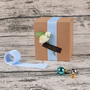 Caja de regalo de kraft marrón con cinta de rayas azul blanco y flor blanca decorativa