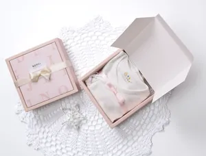 Detailed gift box with newborn striped romper, pink bow, and MERCI tag for baby gifting