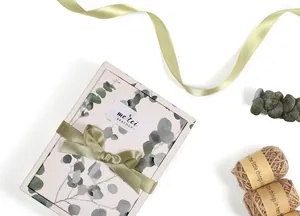 Detail of floral gift box with eucalyptus pattern, olive ribbon, and Merci Beaucoup label