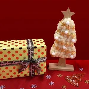 Miniature white wool Christmas tree with gold snowflakes and festive gift box on red background