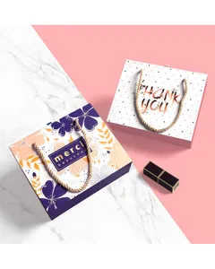 Elegant floral and polka dot gift boxes with gold rope handles on a marble background
