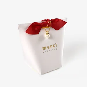Detail of white gift box with red bow, gold charm and pearl accent for wedding favors