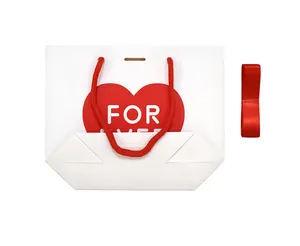Close-up of a white paper gift bag with a red heart design and red woven rope handles