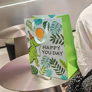 Cartoon green dinosaur gift bag with blue ribbon handle and Happy You Day text