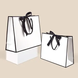 Minimalist white paper gift bags with black borders and silk ribbon handles in two sizes