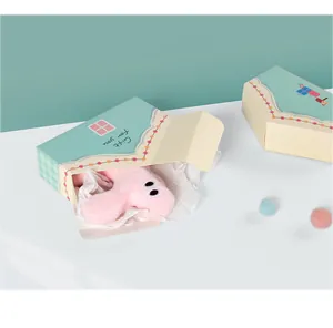Dettaglio di bambola di peluche rosa con occhi grandi e confezione regalo blu pastello
