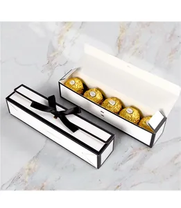 Detail van witte rechthoekige chocolade geschenkdoos met zwart lint en gouden pralines
