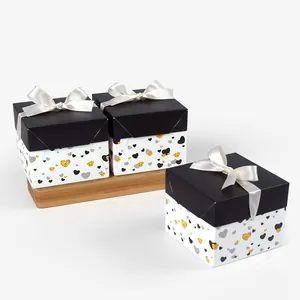 Three square gift boxes with black lids, white heart patterns and white satin bows