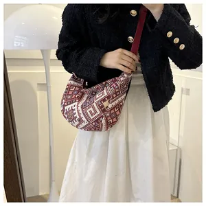 Close-up of geometric patterned dumpling bag with wide red strap on female model