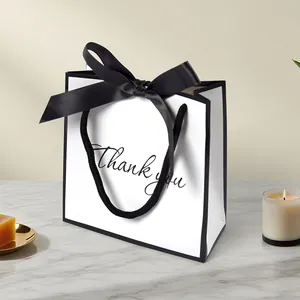 White gift bag with black bow and Thank You text on marble surface with candles