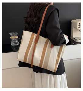 Close-up of striped canvas tote bag with brown leather handles worn over the shoulder
